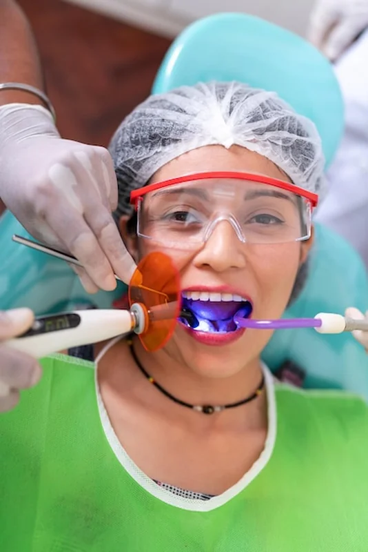 Kobieta poddawana zabiegowi laserowego wybielania zębów w klinice dentystycznej