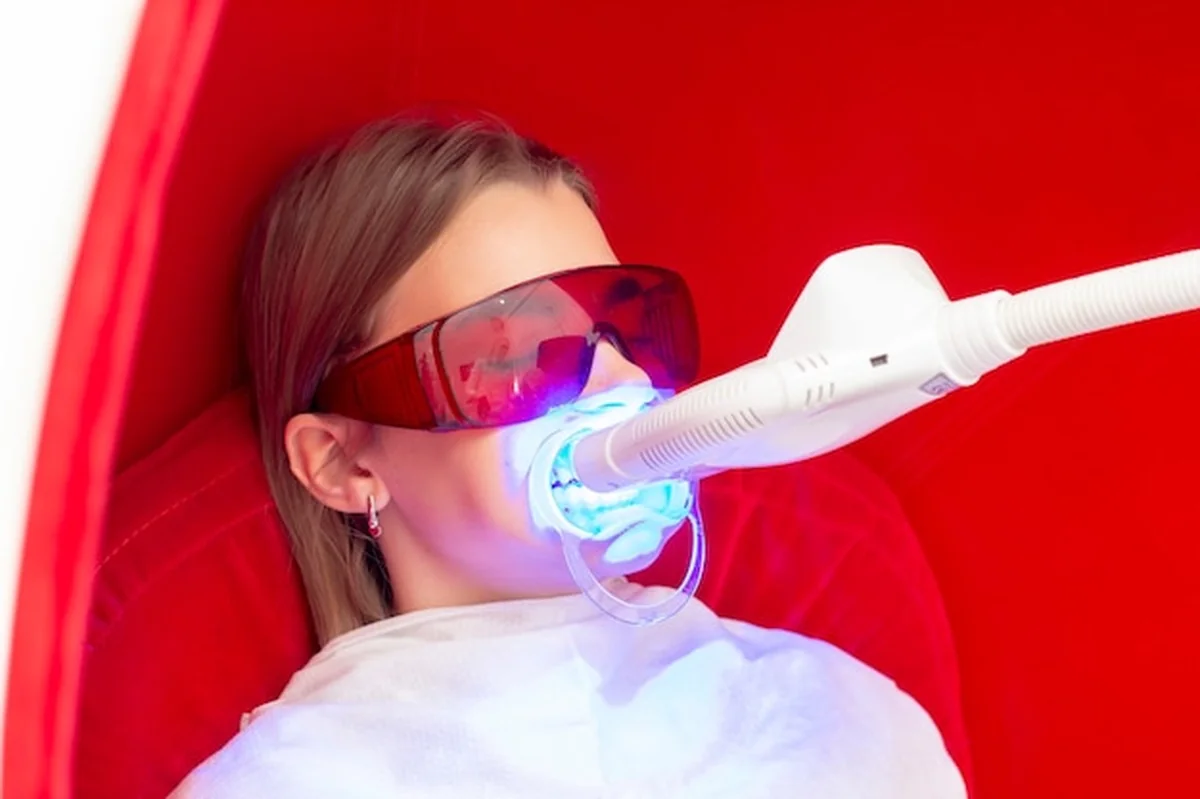 Młoda kobieta wybielająca zęby lampą UV