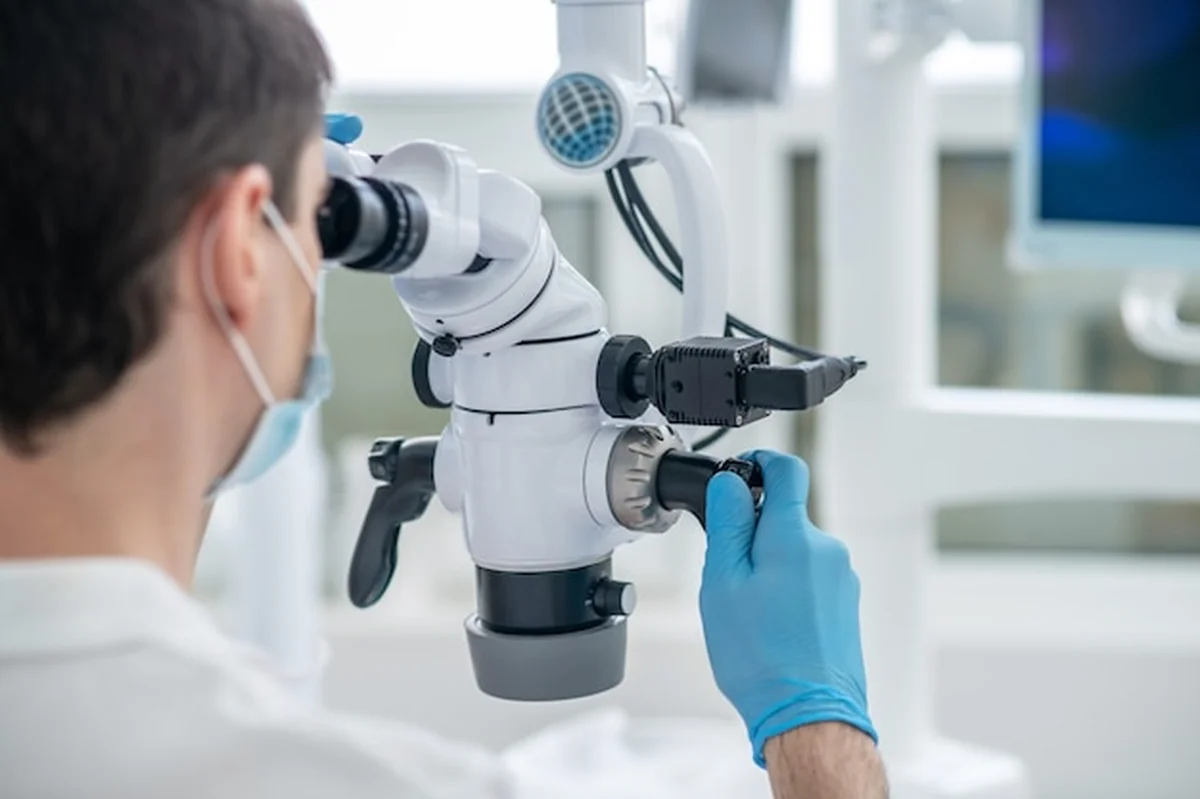 Mężczyzna dentysta wykonuje odbudowę stomatologiczną z użyciem mikroskopu