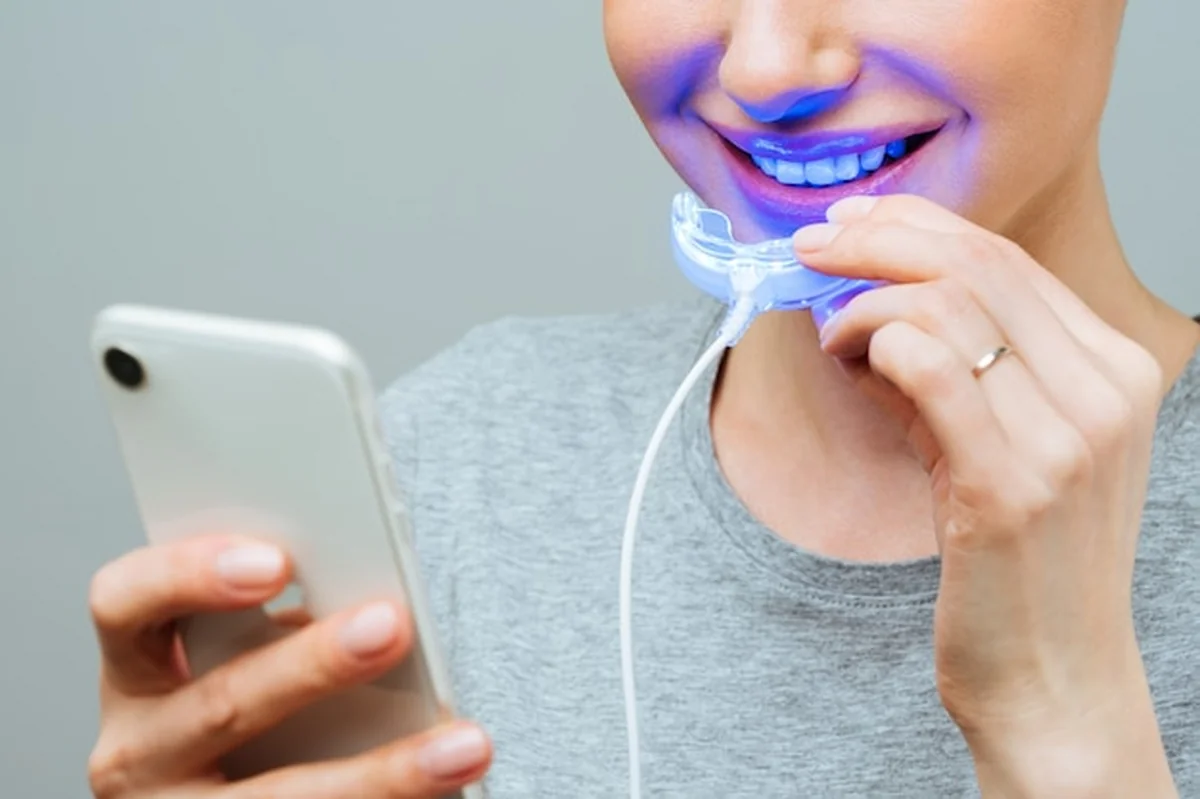 Młoda kobieta wybiela zęby lampą UV w domu